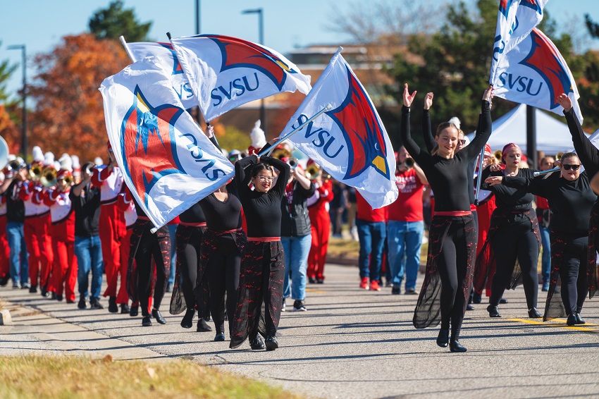 Photo of marching band in the 2024 Homecoming parade. Focusing on the color guard members of the band